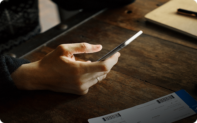 A hand holding a smartphone over a wooden table with papers visible.
